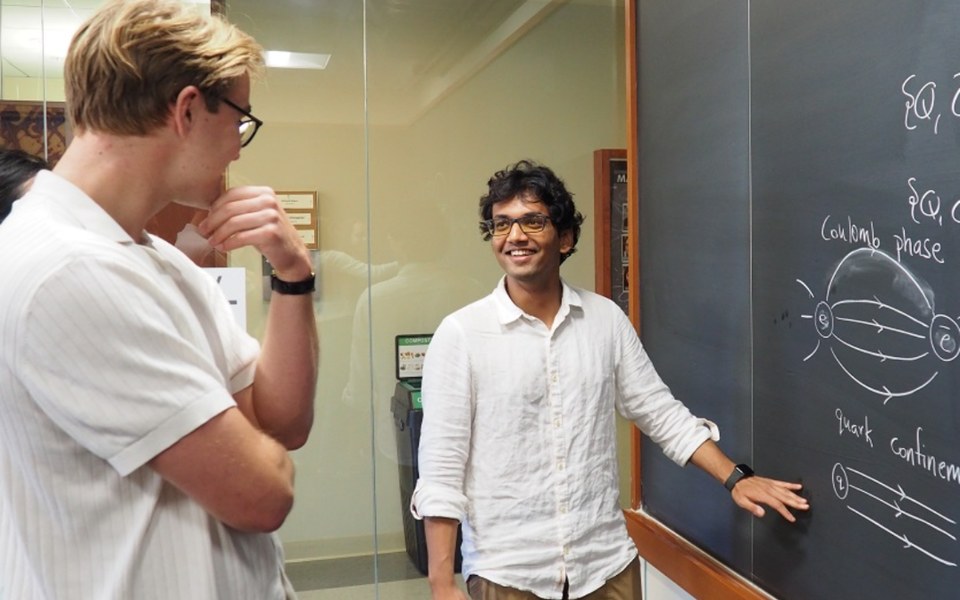 Two young physicists discussing quark confinement at a blackboard